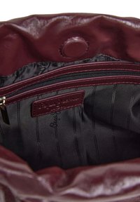 Interno di una borsa in pelle bordeaux con tasca con zip, texture liscia e rivestimento in tessuto con righe verticali. Inclusa etichetta con firma.