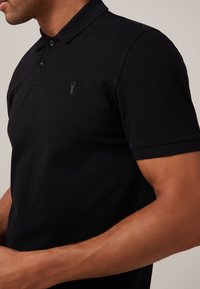 Sort polo t-shirt med et diskret logo på venstre bryst, korte ærmer og en klassisk krave lavet af tekstureret stof.