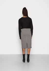 Un pull en maille noir associé à une jupe à carreaux mi-longue avec une fente au dos, complété par des bottes noires à talons.