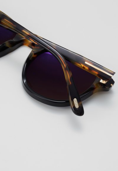 Schildpadzonnebril met donkere lenzen, vlak zwart en bruin patroon, slanke rechthoekige montuur, goudkleurig logo detail op de arm.