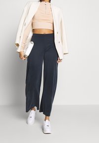 Ljusbeige kort topp med hög krage, tillsammans med vida marinblå byxor. Avslutas med en vit kavaj och vita sneakers.