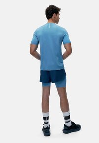 Šviesiai mėlynas trumpas rankovės sportinis marškinėlis su apvaliu kaklu, derinamas su tamsiai mėlynomis šortais. Baigtas juodais sportiniais bateliais ir dryžuotomis kojinėmis.