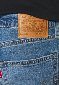 Levi's blå denimjeans med en brun läderlapp märkt "Lot 512," med orange sömmar och två bakfickor.