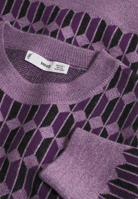 Pull en maille violet avec motif géométrique de losanges noirs et violets foncés, col et poignets côtelés, et une étiquette de vêtement visible à l'intérieur du col.