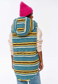 Värviline triibuline vest kapuutsiga, millel on sinine, kollane ja pruun pehme kangas. Pikakese, lohakas disain ümarate servadega.