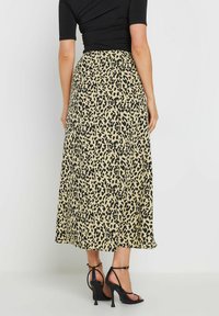 Jupe maxi avec un fond beige présentant un motif léopard noir. Fabriquée en tissu léger, elle a un design fluide et des fentes sur les côtés.