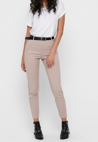 Beige slim-fit housut, joissa on sileä rakenne, sivupaneelit ja musta vyö, yhdistetty valkoiseen kääntöhihaisensa t-paitaan ja mustiin nilkkabootseihin.