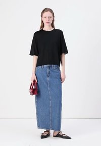 Černý top s krátkým rukávem, modrá maxi sukně s vysokým pasem z denimu, černé ploché boty a malá červená kabelka. Jednoduchý, uvolněný silueta.