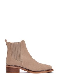 Bottine en suède beige avec panneaux latéraux élastiques, talon marron empilé et languette de traction, présentée de profil sur fond blanc.
