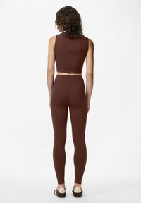 Smeđa krojena bezrukavna majica i usklađene tajice visokog struka, napravljene od glatkog, rastezljivog materijala, prilagođenog kroja, minimalni naglasci.