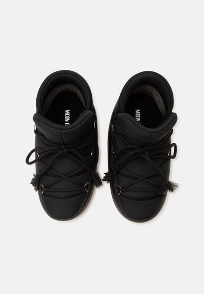 Paire de bottes d'hiver noires matelassées avec des lacets croisés et des cols doux, vues de dessus sur un fond uni.