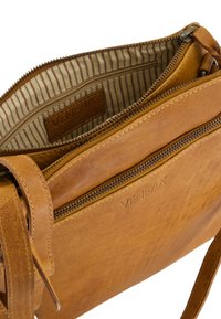 Tan leather crossbody bag with visible zipper pocket and striped fabric interior lining with a brand label inside.