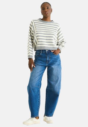 Striped gray and white sweater, cropped design, paired with loose blue jeans. Model wears white sneakers. Simple, casual outfit.