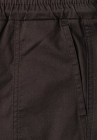 Close-up van een donkerbruine stoffen broekzak met zichtbare stiksels en een elastische tailleband.