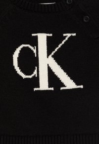 Maglione nero a maglia con un prominente logo bianco "CK". Il design include un col rotondo e dettagli con bottoni sulla spalla.