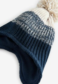 Włóczkowa czapka beanie w kolorze granatowym i kremowym, z prążkowanym wzorem, polarem w środku i dużą pomponem na górze. Miękka tekstura z zapięciem na uszy.