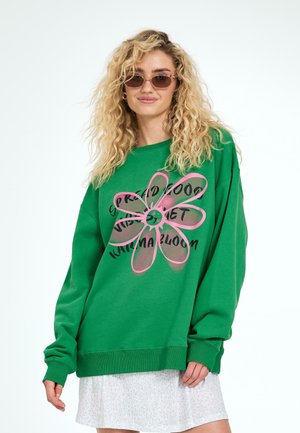 Felpa verde con una grande grafica di un fiore in rosa e testo nero. Presenta maniche lunghe e una vestibilità rilassata. Texture liscia, design casual.