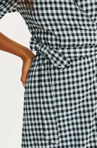 Czarna i biała sukienka w kratkę typu gingham z krótkimi rękawami, wyróżniająca się wiązanym paskiem w talii oraz miękkim, teksturowanym materiałem.