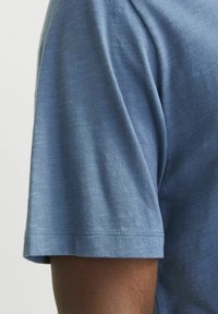Short-sleeved blue cotton T-shirt with a soft texture, featuring straight hem and slightly loose fit, highlighting a subtle heather pattern.