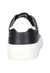 Zapatilla de cuero negra con un acabado texturizado, acento blanco en el talón y detalle del logo en dorado. Suela de goma blanca gruesa para mayor durabilidad.