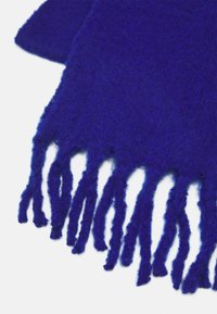 Écharpe bleue foncée et duveteuse avec de longues franges épaisses sur un fond blanc.