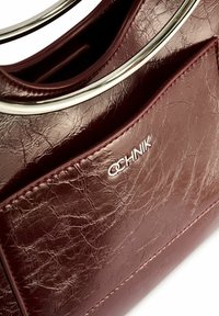 Burgundowa skórzana torebka z teksturowanym wykończeniem, z metalowym uchwytem w kolorze srebrnym oraz przednią kieszenią wytłoczoną z nazwą marki.