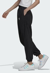 Svarta, lätta joggerbyxor med elastisk midja och sidfickor; har en vit logotyp. Kombineras med vita sneakers med iriserande accenter.