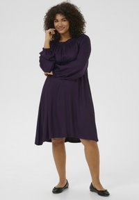 Purple dress with long, puffed sleeves, elastic neckline, and a relaxed silhouette. Worn with black flats. Smooth texture, knee-length.