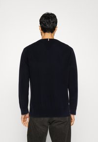 Felpa blu navy in morbido tessuto con scollo a girocollo, maniche lunghe e un piccolo dettaglio rosso e bianco sul retro dello scollo.