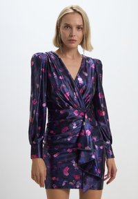 Abito avvolgente in satin viola con motivi floreali in rosa e lilla. Presenta maniche lunghe a sbuffo e un orlo arricciato nella parte inferiore.