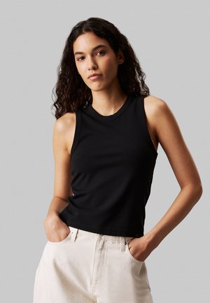 Top nero senza maniche realizzato in morbido tessuto, con scollatura rotonda e design corto. Abbinato a pantaloni di colore chiaro.