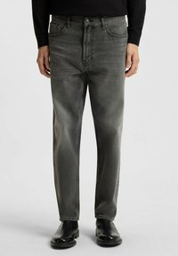 Verbleekte grijze denim jeans met een klassieke pasvorm, voorzien van voorzakken, een knoopsluiting en een gladde textuur, gedragen met zwarte enkelboots.