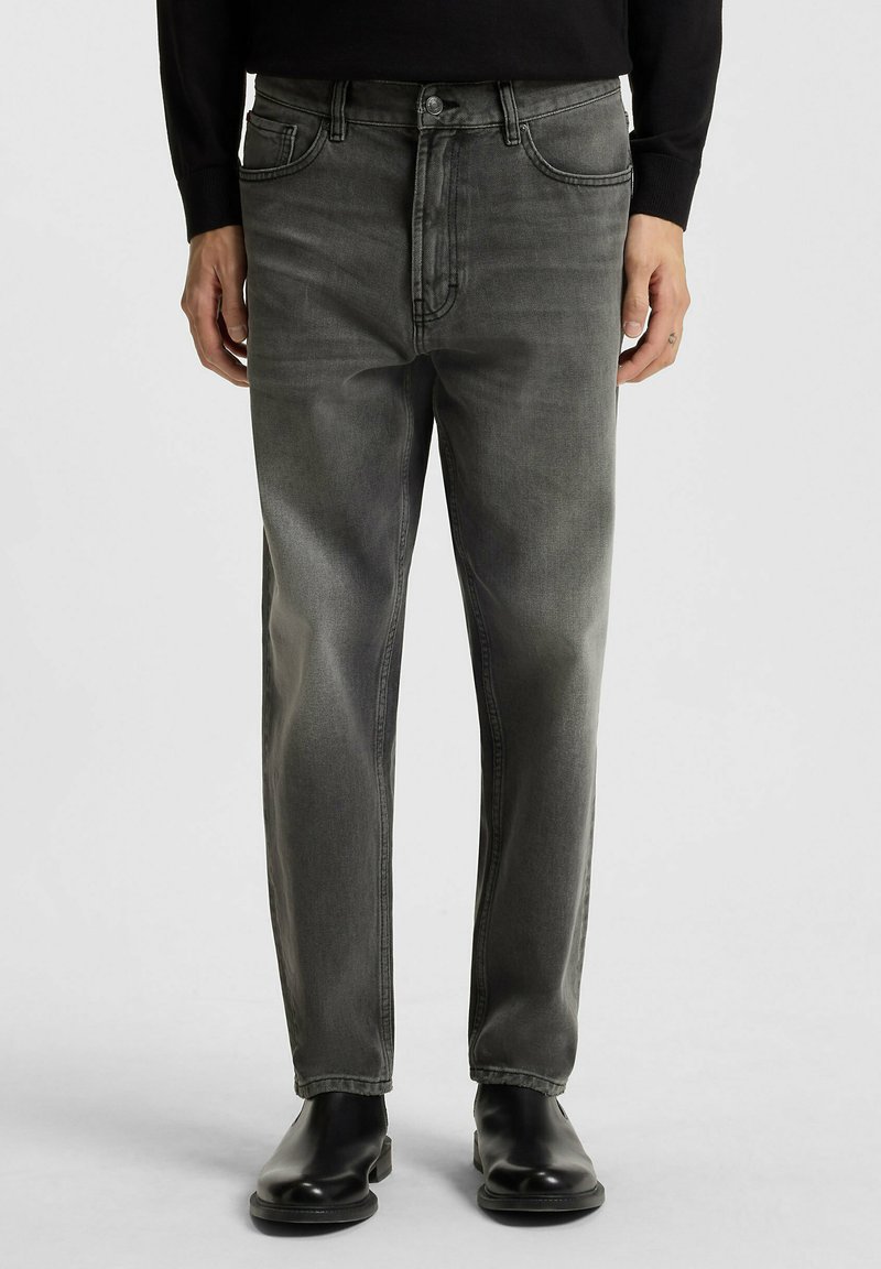 Verbleekte grijze denim jeans met een klassieke pasvorm, voorzien van voorzakken, een knoopsluiting en een gladde textuur, gedragen met zwarte enkelboots.