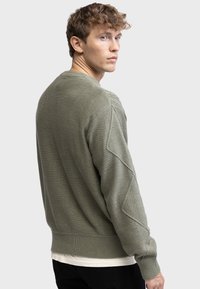 Green knitted sweater featuring textured shoulder accents, ribbed cuffs and hem. The design is casual and tailored with a loose fit.