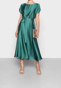 Robe midi en satin bleu canard avec une taille cintrée, des manches courtes et une ceinture à nouer. Assortie à des escarpins argentés à lanières et une pochette métallique.