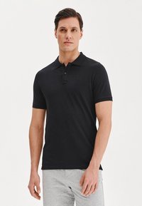 Czarna koszulka polo z krótkimi rękawami, kołnierzykiem i zapięciem na trzy guziki. Gładki materiał i subtelny detal z logo na piersi.