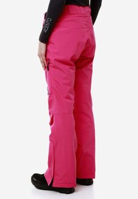 Pantaloni da neve rosa con vita alta, tasche con cerniera e fondo svasato. Il materiale appare impermeabile con una texture liscia.