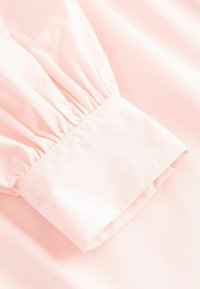 Manche en tissu rose pâle avec un détail élastique froncé près d'un large poignet, montrant une texture lisse et des plis doux.