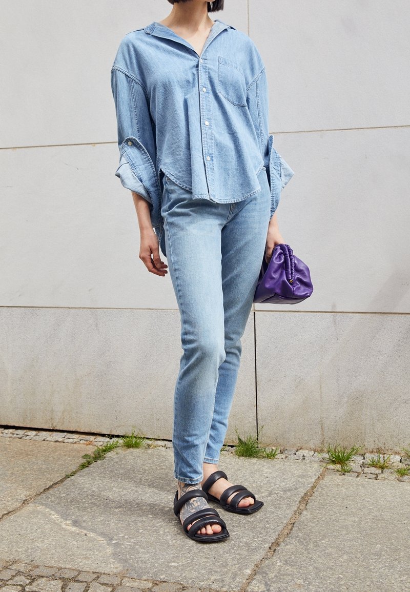 Ljust blå denimskjorta med stora ärmar, matchande ljusblå slim-fit jeans och svarta sandaler med flera remmar. Lila väska i ena handen.