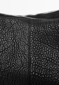 Schwarzes Leder mit genarbter Textur. Verfügt über einen silbernen Reißverschluss entlang der Oberkante, der die kontrastreiche Glätte der Hardware hervorhebt.