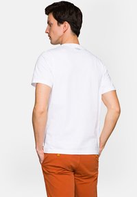 Biała bawełniana koszulka z krótkim rękawem, z okrągłym dekoltem i małym logo marki na górnej części pleców. Połączona z pomarańczowymi spodniami.