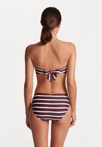 Dviejų dalių bikinis, turintis horizontalių bordo ir baltų dryžių. Viršus yra bandeau stiliaus su užrišama kaspinu nugaroje; apatinė dalis yra vientisa.