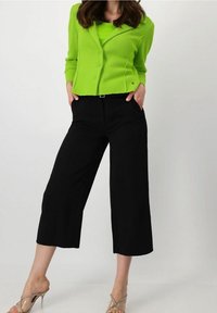 Cardigan de canalé verde claro con dos botones, combinado con pantalones de pierna ancha negros. Textura clara y suave y diseño cortado. Tacones transparentes.