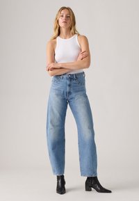 White ribbed tank top, high-waisted light blue denim jeans, and black ankle boots. Jeans feature a relaxed fit and subtle fading.