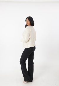 Maglione bianco, texturizzato, con una vestibilità comoda, scollatura rotonda e spalle cadenti, abbinato a jeans neri a campana e scarpe con punta aperta.