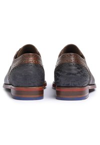 Zapatos de cuero con un cuerpo negro texturizado y acentos marrones con patrones. Suelas gruesas y estratificadas en marrón y rojo con un detalle en azul.