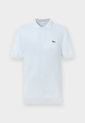 Polo de color azul claro hecho de algodón suave, con un collar clásico, dos botones y un pequeño logo de cocodrilo verde en el pecho.