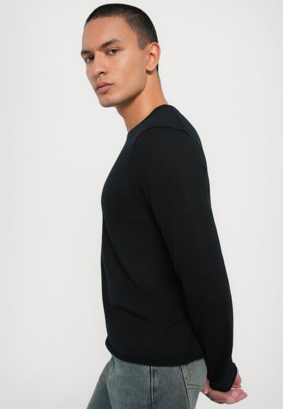 Black long-sleeve sweater in a fitted design, featuring ribbed texture and a crew neckline, paired with light-wash jeans.