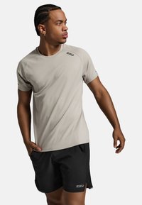 Hele halli lühikeste varrukatega sportlik särk, mis on valmistatud siledast kangast, koos mustade lühikesed pükstega, millel on taskud ja 2XU logo ees.