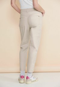 Beiga tapered byxor med bakfickor, som har en slät textur. Matchas med vita sneakers, som har rosa detaljer på hälarna.